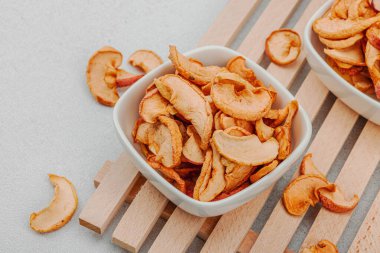 Kuru elma parçalarını kaseye koy. Sağlıklı beslenme, vejetaryen yaşam tarzı, kilo verme konsepti. Beyaz taş beton arka plan, kapat