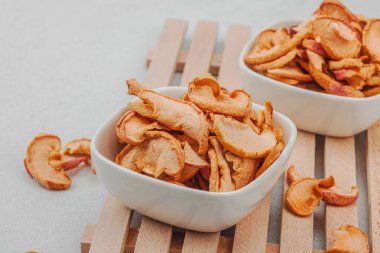 Kuru elma parçalarını kaseye koy. Sağlıklı beslenme, vejetaryen yaşam tarzı, kilo verme konsepti. Beyaz taş beton arka plan, kapat