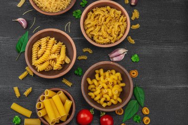 Makarna. Ahşap zemin üzerinde çeşitli pişmemiş makarna ve erişte çeşitleri. Klasik yemek hazırlamak için geleneksel İtalyan malzemesi, sebze ve otlar. Siyah tahtalar, düz yatış, üst manzara