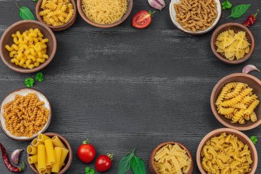 Makarna. Ahşap zemin üzerinde çeşitli pişmemiş makarna ve erişte çeşitleri. Klasik yemek hazırlamak için geleneksel İtalyan malzemesi, sebze ve otlar. Siyah tahtalar, düz yatış, üst manzara