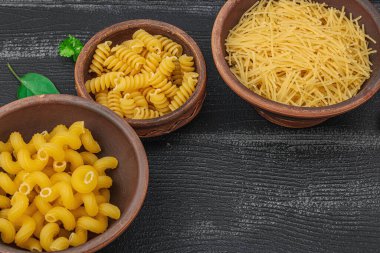 Makarna. Ahşap zemin üzerinde çeşitli pişmemiş makarna ve erişte çeşitleri. Klasik yemek hazırlamak için geleneksel İtalyan malzemesi, sebze ve otlar. Siyah tahtalar, düz yatış, yakın çekim.