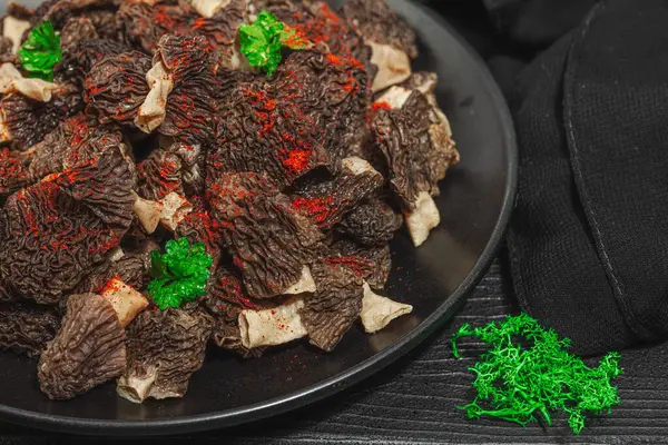 stock image Raw black morel mushrooms with fresh parsley. Vegan ingredient for cooking healthy food. Hobby hunter concept, black wooden background, close up