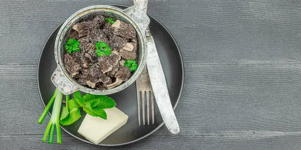 stock image Raw black morel mushrooms with fresh parsley. Vegan ingredient for cooking healthy food. Hobby hunter concept, black wooden background, banner format