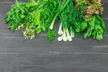 Siyah ahşap arka planda taze yeşillikler ve otlar. Kokulu dereotu, soğan, maydanoz, kuş, marul ve roka. Vejetaryen yemeği, sağlıklı yaşam tarzı, düz yatak, üst manzara.