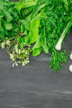 Siyah ahşap arka planda taze yeşillikler ve otlar. Kokulu dereotu, soğan, maydanoz, kuş, marul ve roka. Vejetaryen yemeği, sağlıklı yaşam tarzı, düz yatak, üst manzara.