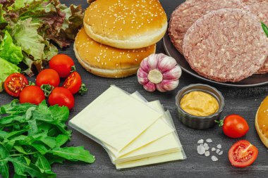 Hamburger köftesi. Sığır pirzolası, çörek, sebze ve sos. Ev yapımı Amerikan klasiği, geleneksel piknik, parti ya da Bağımsızlık Günü yemekleri. Koyu ahşap arka plan, kapat