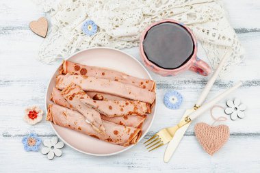 Bir fincan kokulu amber çayı ve kremalı ince krep. İyi ruh hali konsepti, rahat ev konforu. Beyaz ahşap arkaplan, üst görünüm