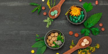 Bitki bazlı takviyeler, taze otlar ve çiçeklerle birlikte doğal vitaminler. Organik ilaçlar bütünsel sağlık kavramlarını, alternatif yaşam tarzını öneriyor. Koyu tahta arkaplan, pankart biçimi