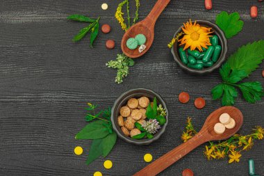Bitki bazlı takviyeler, taze otlar ve çiçeklerle birlikte doğal vitaminler. Organik maddeler, bütünsel sağlık kavramlarını, alternatif yaşam tarzını öneriyor. Koyu ahşap arkaplan, üst manzara