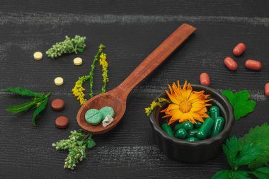 Bitki bazlı takviyeler, taze otlar ve çiçeklerle birlikte doğal vitaminler. Organik maddeler, bütünsel sağlık kavramlarını, alternatif yaşam tarzını öneriyor. Koyu ahşap arka plan, kapat