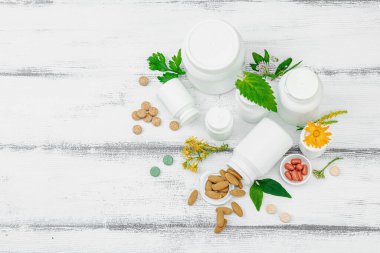 Bitki bazlı takviyeler, taze otlar ve çiçeklerle birlikte doğal vitaminler. Organik maddeler, bütünsel sağlık kavramlarını, alternatif yaşam tarzını öneriyor. Beyaz arkaplan, üst görünüm