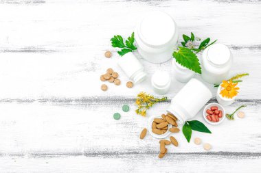 Bitki bazlı takviyeler, taze otlar ve çiçeklerle birlikte doğal vitaminler. Organik maddeler, bütünsel sağlık kavramlarını, alternatif yaşam tarzını öneriyor. Beyaz arkaplan, üst görünüm