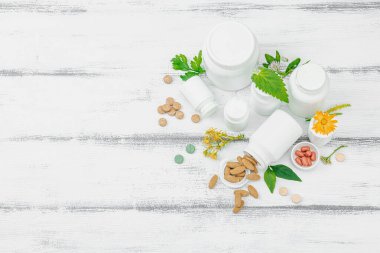 Bitki bazlı takviyeler, taze otlar ve çiçeklerle birlikte doğal vitaminler. Organik maddeler, bütünsel sağlık kavramlarını, alternatif yaşam tarzını öneriyor. Beyaz arkaplan, üst görünüm