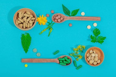 Bitki bazlı takviyeler, taze otlar ve çiçeklerle birlikte doğal vitaminler. Organik maddeler, bütünsel sağlık kavramlarını, alternatif yaşam tarzını öneriyor. Mavi arkaplan, üst görünüm