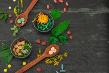 Bitki bazlı takviyeler, taze otlar ve çiçeklerle birlikte doğal vitaminler. Organik maddeler, bütünsel sağlık kavramlarını, alternatif yaşam tarzını öneriyor. Koyu ahşap arkaplan, üst manzara