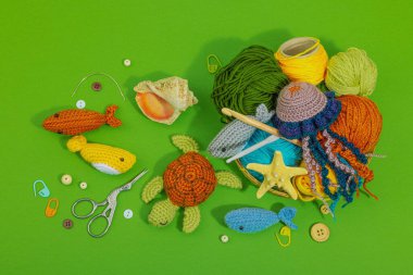 Örgü örmek için bir demet iplik. Farklı sualtı hayvanları, el yapımı deniz hobisi. Yeşil arkaplan, üst görünüm özel sanatlar araçları