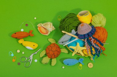 Örgü örmek için bir demet iplik. Farklı sualtı hayvanları, el yapımı deniz hobisi. Yeşil arkaplan, üst görünüm özel sanatlar araçları