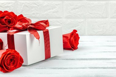 Beyaz arka planda hediye kutusu olan bir buket kırmızı gül. Çiçek açan, Anneler Günü ya da Sevgililer Günü için neşeli bir konsept. Tebrik kartı, Paskalya düzlüğü, en iyi dileklerimle, kopyalama alanı