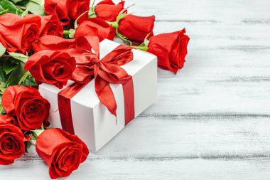 Beyaz arka planda hediye kutusu olan bir buket kırmızı gül. Çiçek açan, Anneler Günü ya da Sevgililer Günü için neşeli bir konsept. Tebrik kartı, Paskalya düzlüğü, en iyi dileklerimle, kopyalama alanı