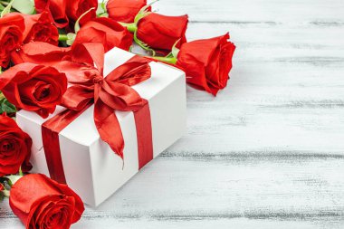 Beyaz arka planda hediye kutusu olan bir buket kırmızı gül. Çiçek açan, Anneler Günü ya da Sevgililer Günü için neşeli bir konsept. Tebrik kartı, Paskalya düzlüğü, en iyi dileklerimle, kopyalama alanı
