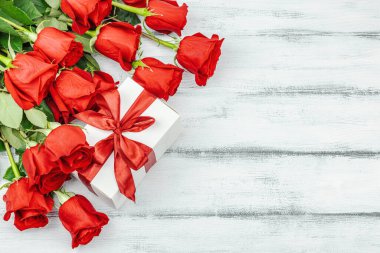 Beyaz arka planda hediye kutusu olan bir buket kırmızı gül. Çiçek açan, Anneler Günü ya da Sevgililer Günü için neşeli bir konsept. Tebrik kartı, Paskalya düzlüğü, en iyi dilekler, en iyi manzara.