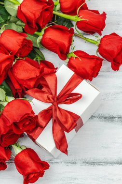 Beyaz arka planda hediye kutusu olan bir buket kırmızı gül. Çiçek açan, Anneler Günü ya da Sevgililer Günü için neşeli bir konsept. Tebrik kartı, Paskalya düzlüğü, en iyi dilekler, en iyi manzara.
