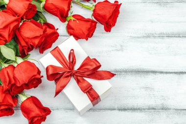 Beyaz arka planda hediye kutusu olan bir buket kırmızı gül. Çiçek açan, Anneler Günü ya da Sevgililer Günü için neşeli bir konsept. Tebrik kartı, Paskalya düzlüğü, en iyi dilekler, en iyi manzara.