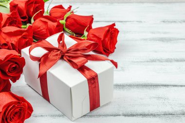 Beyaz arka planda hediye kutusu olan bir buket kırmızı gül. Çiçek açan, Anneler Günü ya da Sevgililer Günü için neşeli bir konsept. Tebrik kartı, Paskalya düzlüğü, en iyi dileklerimle, kopyalama alanı