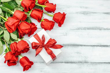 Beyaz arka planda hediye kutusu olan bir buket kırmızı gül. Çiçek açan, Anneler Günü ya da Sevgililer Günü için neşeli bir konsept. Tebrik kartı, Paskalya düzlüğü, en iyi dilekler, en iyi manzara.