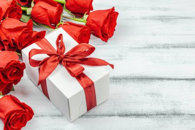 Beyaz arka planda hediye kutusu olan bir buket kırmızı gül. Çiçek açan, Anneler Günü ya da Sevgililer Günü için neşeli bir konsept. Tebrik kartı, Paskalya düzlüğü, en iyi dileklerimle, kopyalama alanı