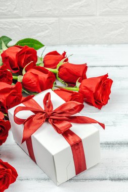 Beyaz arka planda hediye kutusu olan bir buket kırmızı gül. Çiçek açan, Anneler Günü ya da Sevgililer Günü için neşeli bir konsept. Tebrik kartı, Paskalya düzlüğü, en iyi dileklerimle, kopyalama alanı