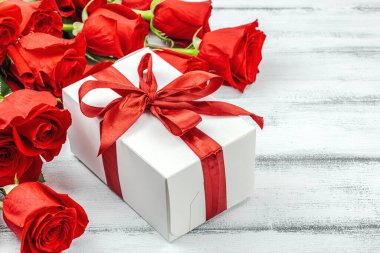 Beyaz arka planda hediye kutusu olan bir buket kırmızı gül. Çiçek açan, Anneler Günü ya da Sevgililer Günü için neşeli bir konsept. Tebrik kartı, Paskalya düzlüğü, en iyi dileklerimle, kopyalama alanı