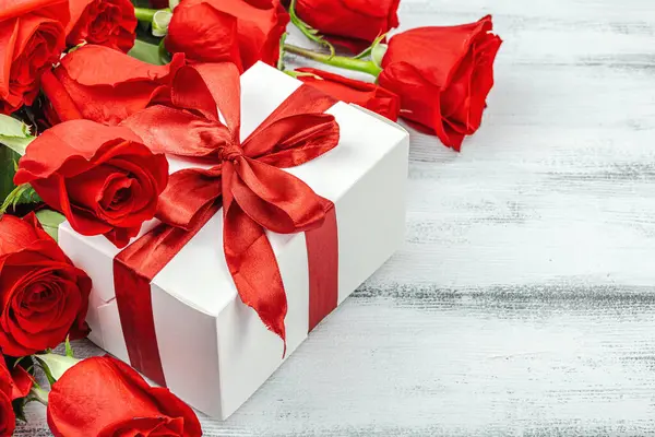 Beyaz arka planda hediye kutusu olan bir buket kırmızı gül. Çiçek açan, Anneler Günü ya da Sevgililer Günü için neşeli bir konsept. Tebrik kartı, Paskalya düzlüğü, en iyi dileklerimle, kopyalama alanı
