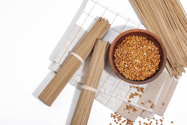 Japanese buckwheat soba noodles. Classic ingredient for preparing traditional dishes. Ceramic bowl, linen napkin. Hard light, dark shadow, white background, top view clipart