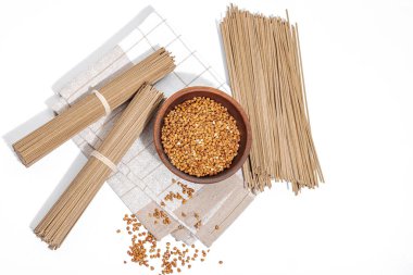 Japanese buckwheat soba noodles. Classic ingredient for preparing traditional dishes. Ceramic bowl, linen napkin. Hard light, dark shadow, white background, top view clipart