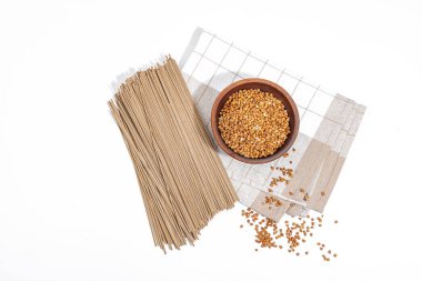 Japanese buckwheat soba noodles. Classic ingredient for preparing traditional dishes. Ceramic bowl, linen napkin. Hard light, dark shadow, white background, top view clipart