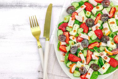 Çilekli taze salata, yapraklar, peynir, olgun üzüm ve füme tavuk. Haşhaş tohumlu leziz bir sos, geleneksel sağlıklı yiyecek yaşam tarzı. Beyaz ahşap arkaplan, üst görünüm