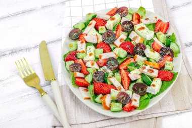 Çilekli taze salata, yapraklar, peynir, olgun üzüm ve füme tavuk. Haşhaş tohumlu leziz bir sos, geleneksel sağlıklı yiyecek yaşam tarzı. Beyaz ahşap arka plan, kapat