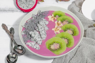 Meyve, kivi, muz ve haşhaş tohumlu Pitaya smoothie kasesi. Moda yemek, sağlıklı kahvaltı fikri. Sert ışık, karanlık gölge, beyaz ahşap zemin, kapat