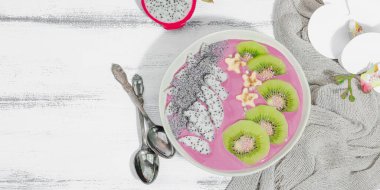 Meyve, kivi, muz ve haşhaş tohumlu Pitaya smoothie kasesi. Moda yemek, sağlıklı kahvaltı fikri. Sert ışık, koyu gölge, beyaz ahşap arkaplan, afiş biçimi