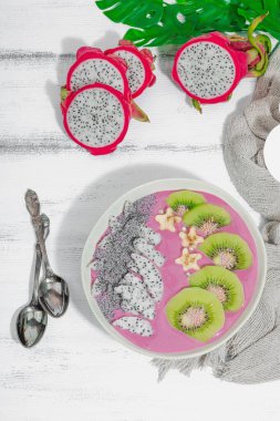 Meyve, kivi, muz ve haşhaş tohumlu Pitaya smoothie kasesi. Moda yemek, sağlıklı kahvaltı fikri. Sert ışık, karanlık gölge, beyaz ahşap zemin, üst manzara