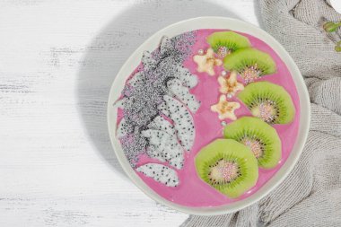 Meyve, kivi, muz ve haşhaş tohumlu Pitaya smoothie kasesi. Moda yemek, sağlıklı kahvaltı fikri. Sert ışık, karanlık gölge, beyaz ahşap zemin, üst manzara