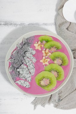 Meyve, kivi, muz ve haşhaş tohumlu Pitaya smoothie kasesi. Moda yemek, sağlıklı kahvaltı fikri. Sert ışık, karanlık gölge, beyaz ahşap zemin, üst manzara