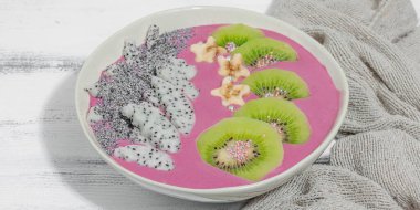 Meyve, kivi, muz ve haşhaş tohumlu Pitaya smoothie kasesi. Moda yemek, sağlıklı kahvaltı fikri. Sert ışık, koyu gölge, beyaz ahşap arkaplan, afiş biçimi