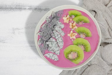 Meyve, kivi, muz ve haşhaş tohumlu Pitaya smoothie kasesi. Moda yemek, sağlıklı kahvaltı fikri. Sert ışık, karanlık gölge, beyaz ahşap zemin, üst manzara