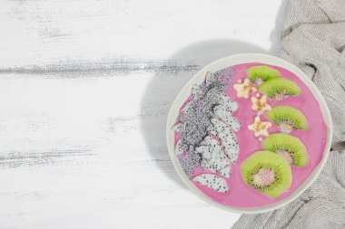 Meyve, kivi, muz ve haşhaş tohumlu Pitaya smoothie kasesi. Moda yemek, sağlıklı kahvaltı fikri. Sert ışık, karanlık gölge, beyaz ahşap zemin, üst manzara