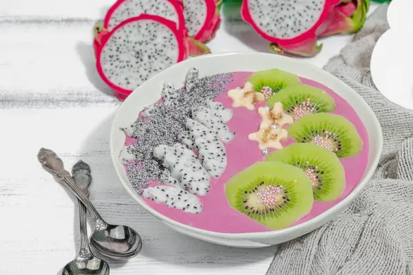 Meyve, kivi, muz ve haşhaş tohumlu Pitaya smoothie kasesi. Moda yemek, sağlıklı kahvaltı fikri. Sert ışık, karanlık gölge, beyaz ahşap zemin, kapat