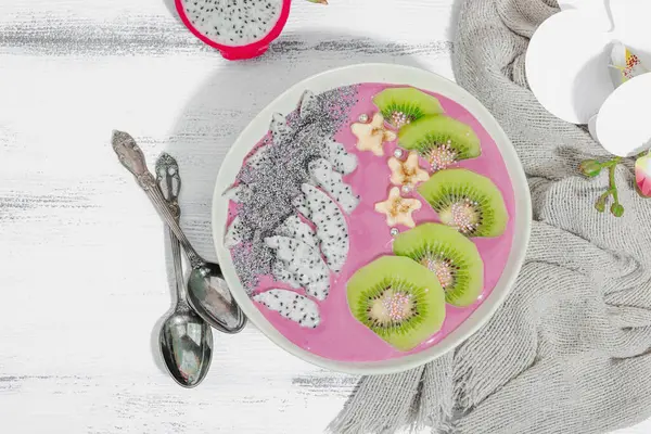 Meyve, kivi, muz ve haşhaş tohumlu Pitaya smoothie kasesi. Moda yemek, sağlıklı kahvaltı fikri. Sert ışık, karanlık gölge, beyaz ahşap zemin, üst manzara