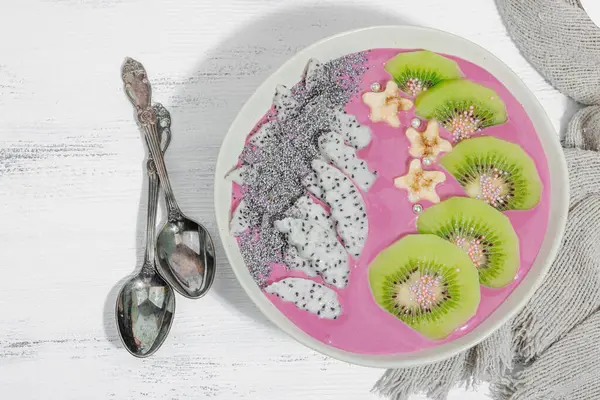 Meyve, kivi, muz ve haşhaş tohumlu Pitaya smoothie kasesi. Moda yemek, sağlıklı kahvaltı fikri. Sert ışık, karanlık gölge, beyaz ahşap zemin, üst manzara