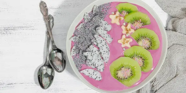 Meyve, kivi, muz ve haşhaş tohumlu Pitaya smoothie kasesi. Moda yemek, sağlıklı kahvaltı fikri. Sert ışık, karanlık gölge, beyaz ahşap zemin, üst manzara